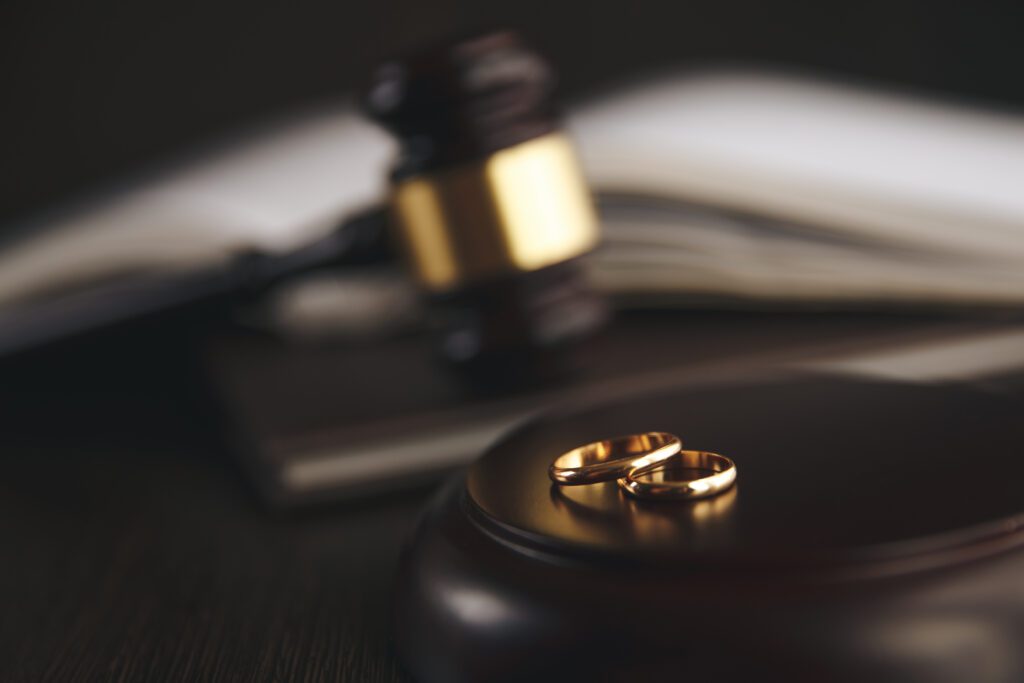 Two gold rings on a wooden surface with a judge's gavel and an open book in the blurred background.