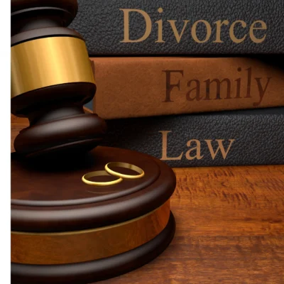 A judge's gavel and two wedding rings sit on a wooden table beside books labeled "Divorce," "Family," and "Law.
